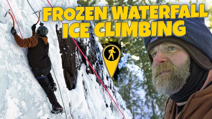 A lone ice climber ascends a towering, blue-tinted frozen waterfall, surrounded by snow-covered rock faces. The climber is equipped with professional gear and the ice reflects light, creating a surreal, beautiful scene. This image showcases the challenge and beauty of ice climbing in the Canadian Rockies.