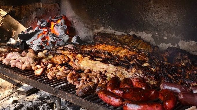Close-up shot of Asado grilling on the parrilla, with the flames visible and the meat sizzling. Focus on texture, contrast, and vibrant colors.