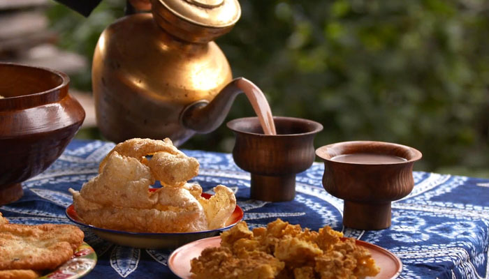 A scenic overlook of a partially dirt, partially snow road in the Tian Shan Mountains during a sunny day.