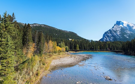 A fat biker riding along the snow-covered Bow River Trail with Cascade Mountain in the background, with frozen bubbles on the surface of the partially frozen Bow River visible in the foreground.