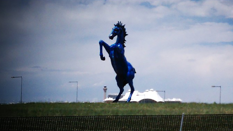 A close-up shot of the Blue Mustang's head, emphasizing the texture of the fiberglass and the piercing red LED eyes.