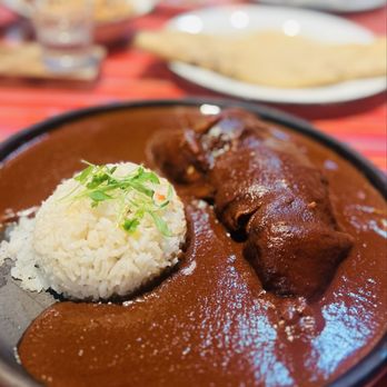 A deep, dark bowl of Mole Negro, garnished with sesame seeds and herbs.
