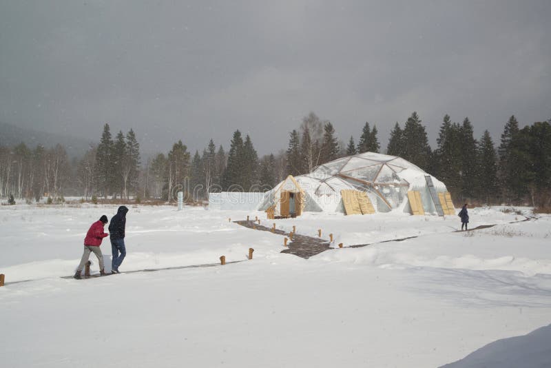 A Buryat woman in traditional clothing smiles, holding a freshly caught fish on the ice of Lake Baikal.