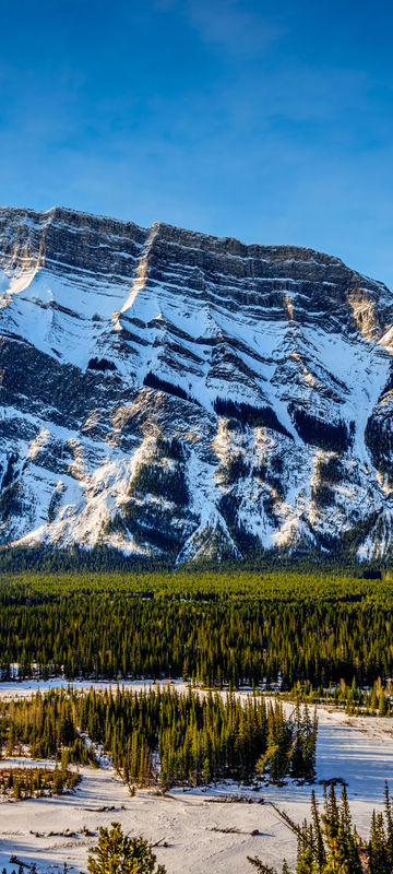 A winter scene in Banff National Park, Alberta, Canada, showing the snow-covered landscape and mountains under a clear blue sky. This image represents the quintessential beauty of the Canadian Rockies in winter.