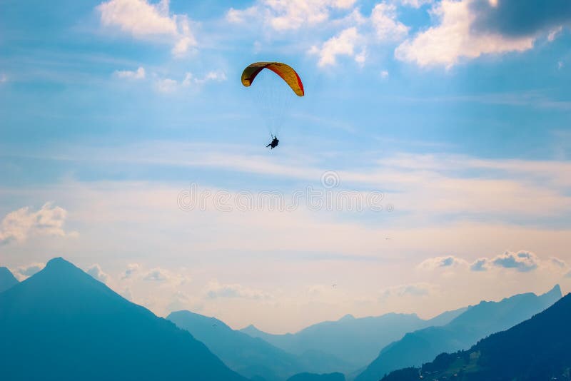 A paraglider silhouetted against a vibrant sunset over the Swiss Alps, shot with a shallow depth of field to emphasize the subject. The lighting is warm and inviting, capturing the golden hour glow.