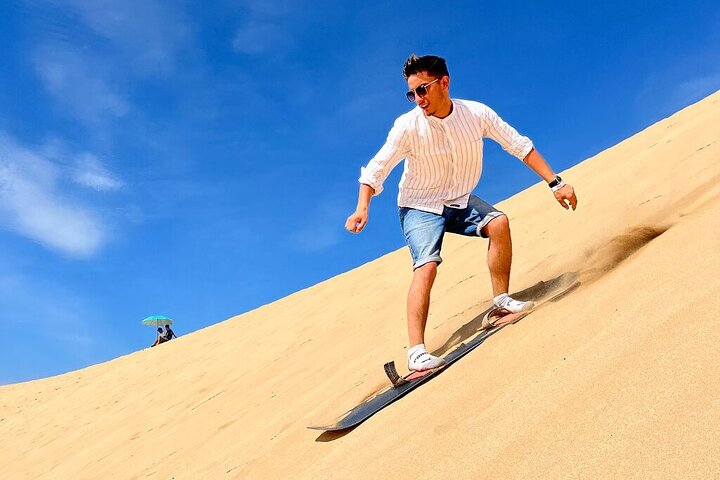Sandboarding in Huacachina Peru, a person carving down a large dune with the oasis visible in the distance