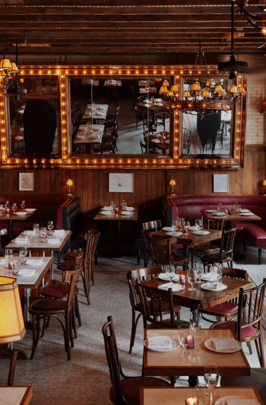 A stylish room at The Ludlow Hotel, showcasing the exposed brick, velvet furnishings, and floor-to-ceiling windows with a city view.