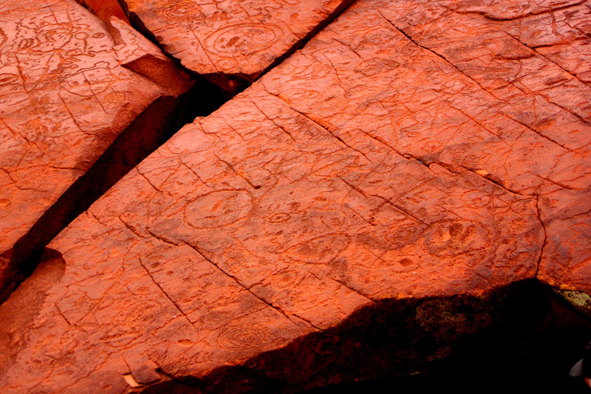 Wide shot of Uluru with visible rock art markings, perhaps partially obscured in shadow for dramatic effect.
