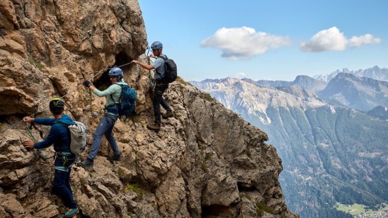 Via Ferrata in the Italian Dolomites: A climber secured to a steel cable on a rocky cliff, showcasing the blend of hiking and climbing with breathtaking mountain views in the background.