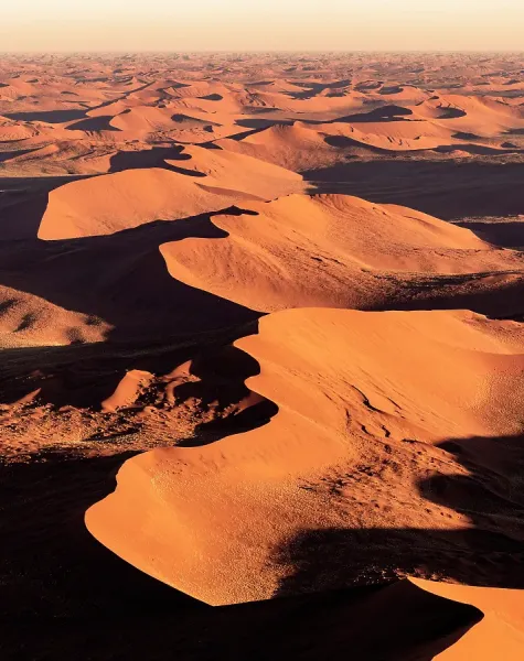 Towering red dunes of Sossusvlei against a clear blue sky in the Namib Desert, Namibia, showcasing the stark contrast and immensity of the landscape.
