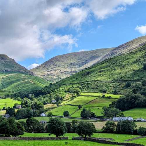 A calm lake reflects the surrounding mountains, with a lone kayaker gently paddling across the surface. The scene evokes a sense of peace and tranquility.