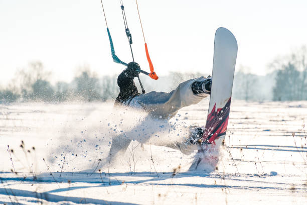 Wide shot of a snowkiter silhouetted against a backdrop of snow-covered fields and distant mountains under a brilliant blue sky. A snowkiter navigates a windswept Hokkaido field, showcasing the expansive, snow-covered landscape perfect for this exhilarating sport.