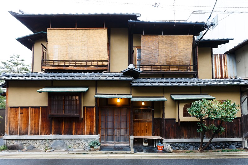 The exterior of a traditional Machiya townhouse, showcasing its wooden latticework and tiled roof. This style of accommodation offers an authentic Kyoto experience and a glimpse into the city's past.