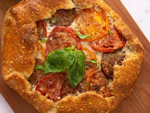 Fresh basil leaves scattered around a weathered wooden table, adding aromatic elegance to the scene, complementing the galette.
