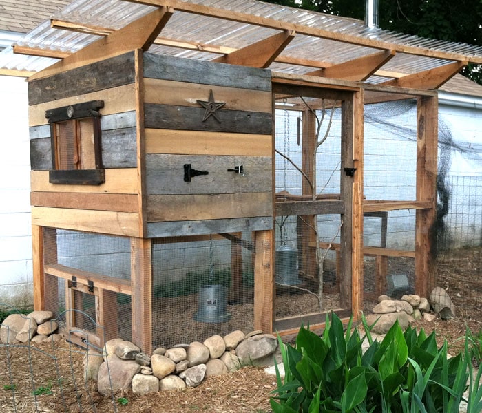 Exterior view of the chicken coop partially enclosed with reclaimed pallet lumber, showing varying textures and colors, soft morning light.