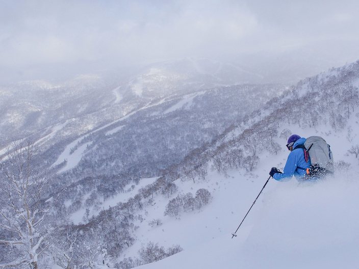 A snowboarder navigates through deep powder snow in the backcountry of Hokkaido, Japan, encapsulating the sense of freedom and adventure amidst a pristine winter landscape.