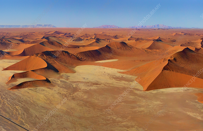 A photographer stands under a star-filled sky in the Namib Desert, setting up equipment for long-exposure astrophotography, illustrating the dedication required to capture the night sky.