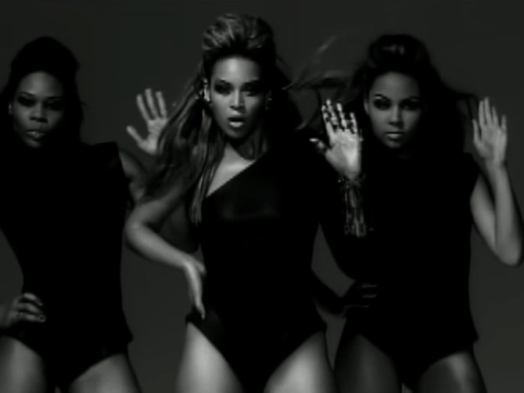 Dancers in stark white spotlights form a precise pyramid shape behind Beyoncé during her 
