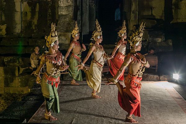 Apsara dancers in traditional costumes performing a dance with elaborate hand gestures under soft lighting, illustrating cultural immersion and support for local arts.