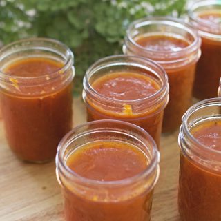 A person holds a jar of freshly canned pizza sauce