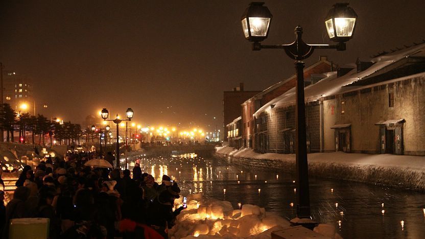 Envision this: A long exposure photo of the Otaru Canal, bathed in the warm, yellow light of the snow lanterns, with blurred reflections creating a dreamy, romantic atmosphere.