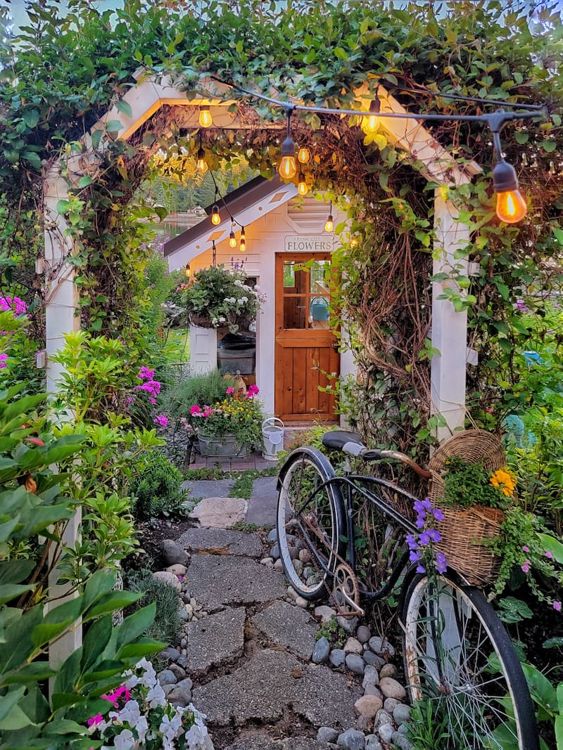 A charming greenhouse with a winding stone path surrounded by lush greenery, demonstrating a blend of functionality and farmhouse aesthetics.