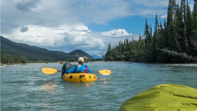 Packrafter paddling down a river with mountains in the background