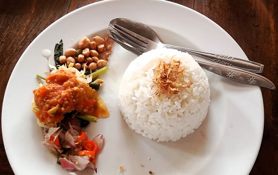 A group of people preparing food in a Balinese cooking class with rice fields in the background.