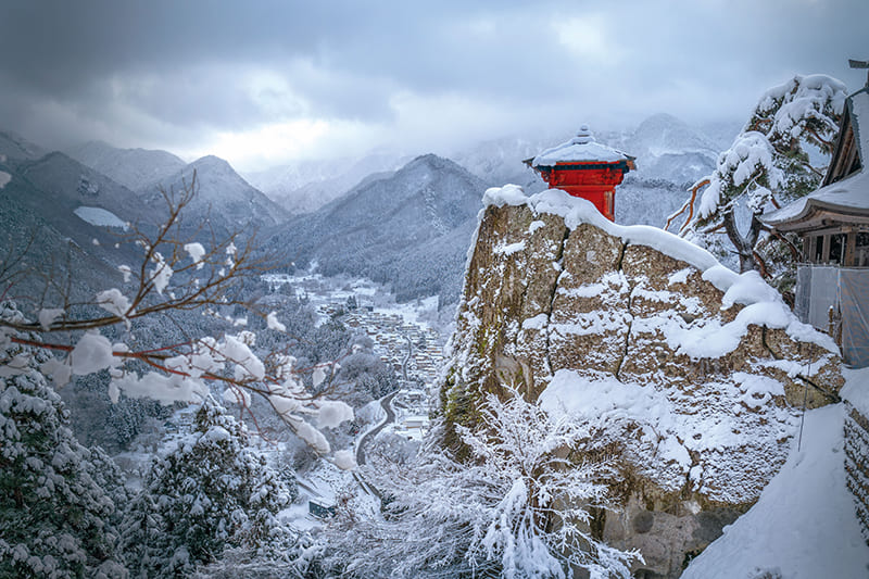 A dramatic wide shot from the Asahidake Ropeway, showcasing the vast expanse of snow-covered mountains and valleys below, with the ropeway cables prominently in the foreground.