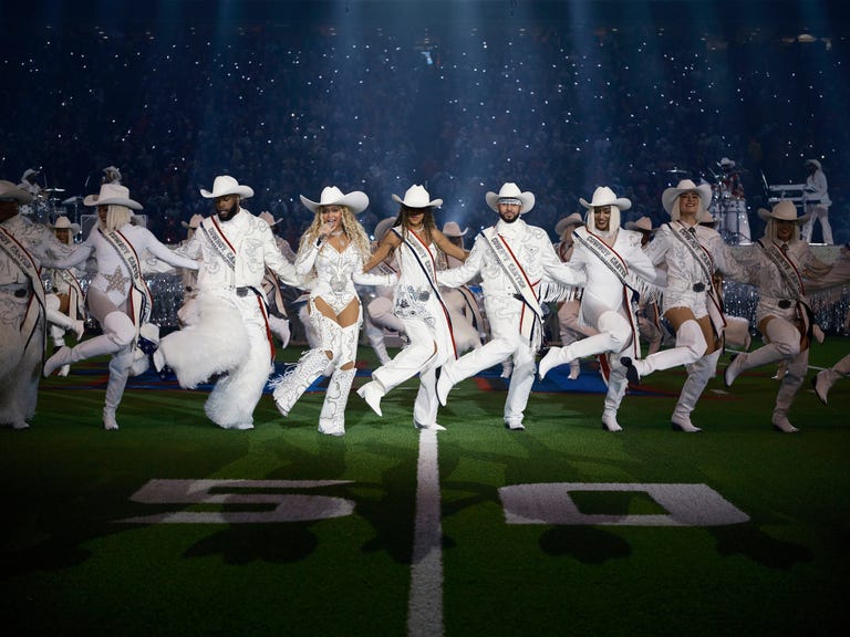 Beyoncé silhouetted against a dramatic backdrop of swirling lights and smoke during her Super Bowl Halftime performance.