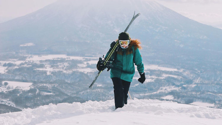 Steam rises from the thermal waters of an onsen in Noboribetsu's Jigokudani (Hell Valley), surrounded by snow-covered rocks and a vibrant landscape, highlighting the relaxation and mineral-rich experience of onsen hopping.