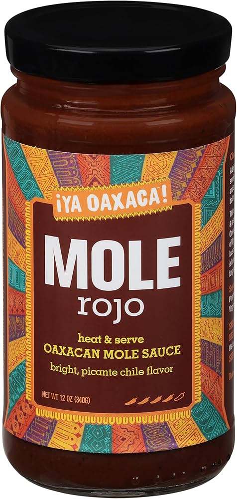 An overhead shot of mole negro sauce, glistening dark brown in a serving dish, garnished with sesame seeds and fresh herbs.