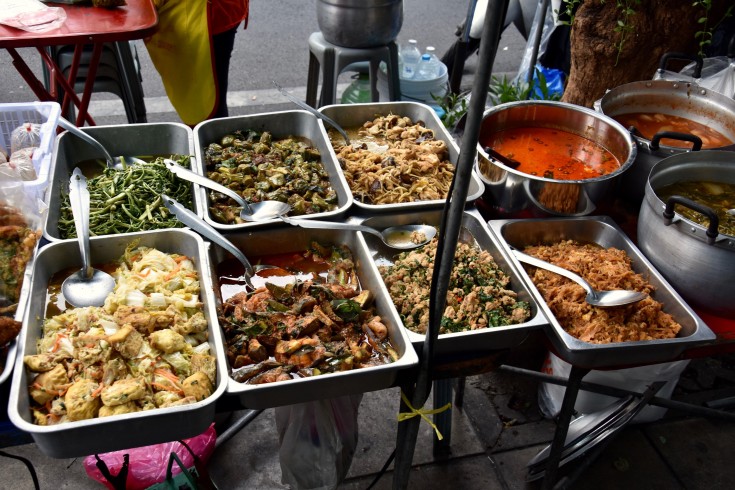 A close-up, almost macro shot of the Pad Thai being prepared by the old woman with the blue apron at the Sala Daeng BTS station night market, focusing on the sizzling wok and the vendor's skillful hands. Sharp focus and vibrant colors are essential.