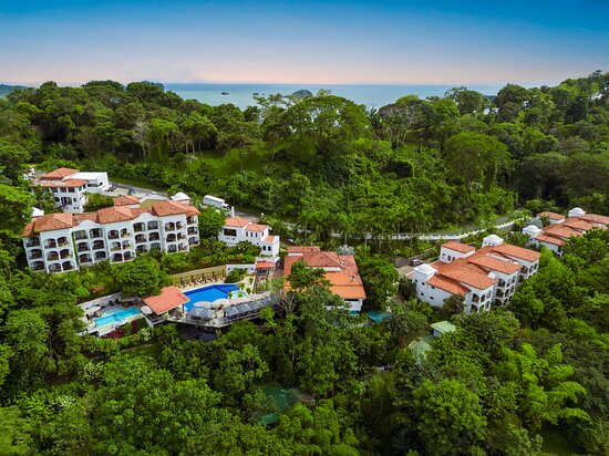 A family carefully searching for fossils amongst the rocks on Durdle Door Beach. The parents are helping their children use small hammers and chisels to gently excavate fossils, while other families are visible in the background, enjoying the scenery.