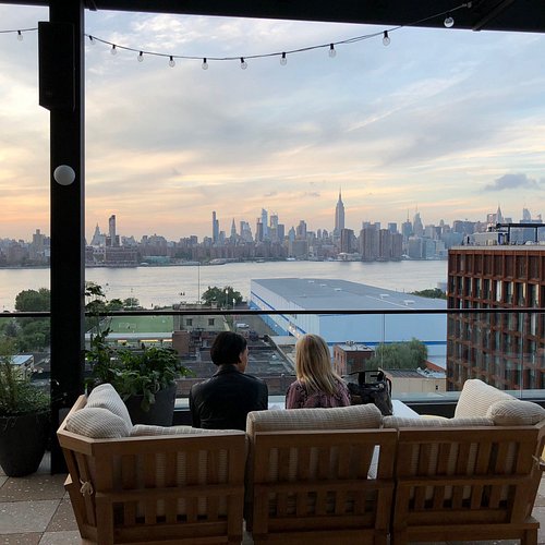 A guest room at The Hoxton, Williamsburg featuring the bed, mid-century modern furniture, and curated in-room books