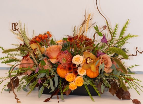 A beautiful fall table centerpiece featuring an assortment of gourds, candles, and autumn foliage arranged on a wooden table.
