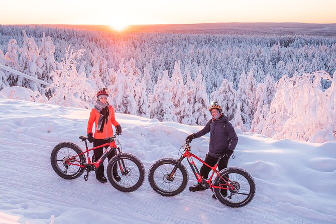 Two individuals driving snowmobiles through a snow-covered forest.