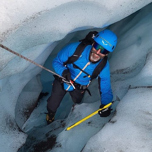 Action shot of adventurers descending into a glacial crevasse in Skaftafell Glacier, emphasizing the icy blue color and scale.