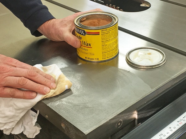 A close-up view shows a hand scrubbing a cast iron skillet with a salt and oil mixture, using a natural bristle brush. The focus is on the texture and the action of cleaning.