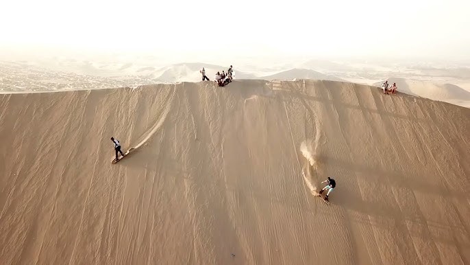 Sandboarding in Huacachina, Peru, showcasing the towering dunes and the vibrant oasis in the background