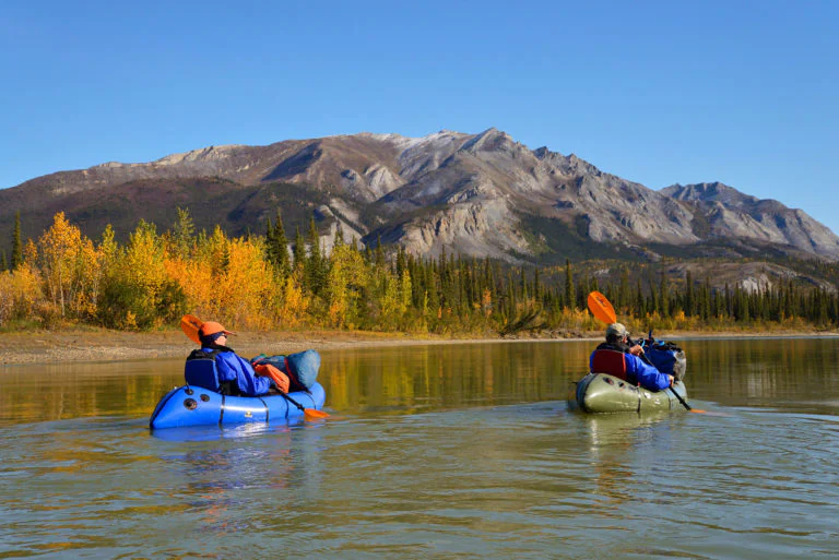 A packrafter paddles down a river in the Gates of the Arctic National Park, with the rugged mountains and vast wilderness stretching out in the distance.