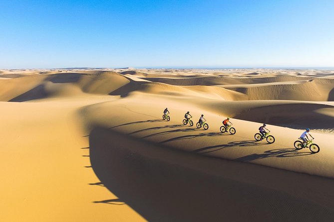 A person fat-tire biking down a massive sand dune in the Namib Desert at golden hour, showcasing the vastness and beauty of the landscape.