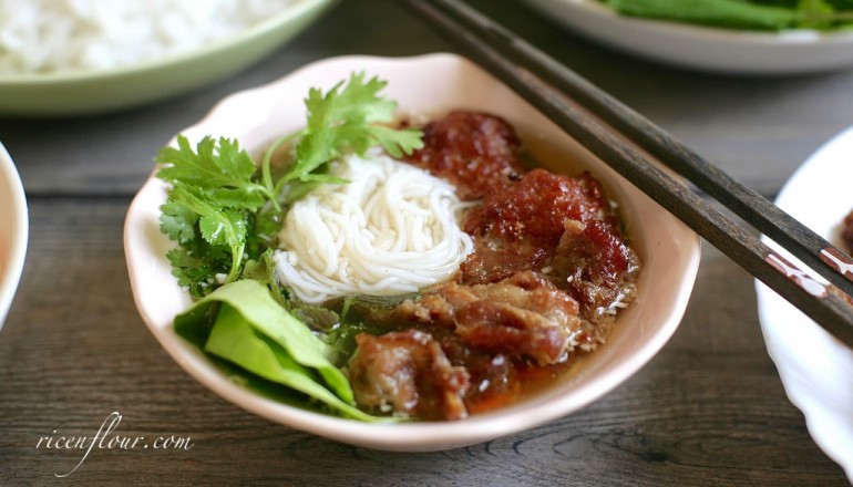 A plate of Bun Cha, showing the grilled pork patties, rice noodles, herbs, and dipping sauce. The alt text describes Bun Cha as featuring grilled pork patties in broth, rice noodles, fresh herbs, and a side of nuoc cham dipping sauce.