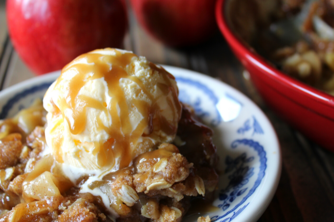Crisp topping being sprinkled over the apple filling in the baking dish.
