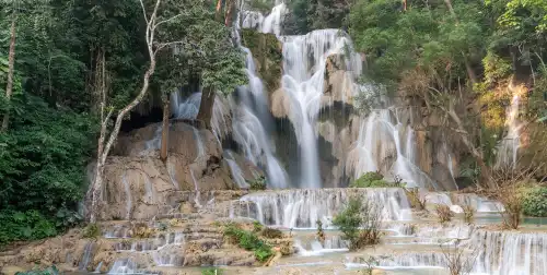 Kuang Si Falls near Luang Prabang, showcasing the multi-tiered waterfalls and the turquoise-colored pools. Visitors are seen swimming and enjoying the natural beauty.