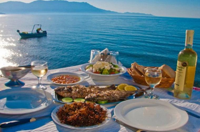 A sleek, white catamaran sails on a calm, turquoise sea in the Greek Islands, bathed in warm sunlight.