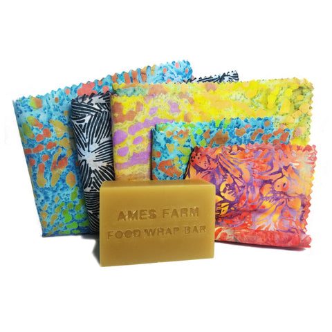Overhead shot of a rustic wooden table covered with colorful beeswax food wraps in various sizes and patterns. Some of the wraps are folded, while others are wrapped around ceramic bowls containing leftovers.