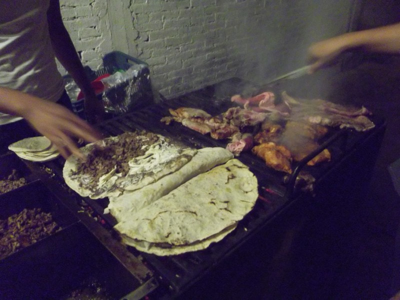 A Tlayuda being assembled by a vendor in a street food market, showing the vibrant colors and textures of the ingredients under warm evening light.