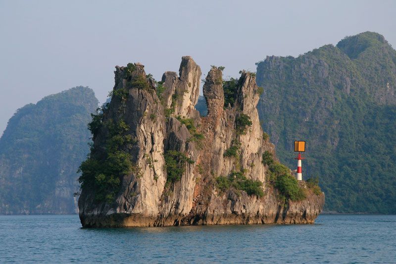 A stunning overhead view of Ha Long Bay showing numerous limestone karsts rising from the water under a clear blue sky. The scene emphasizes the vastness and beauty of the landscape, perfect for a luxury travel blog.