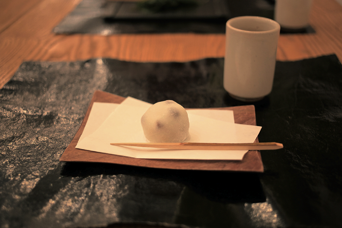 Hand of a craftsman prepares traditional wagashi in a sunlit kitchen.